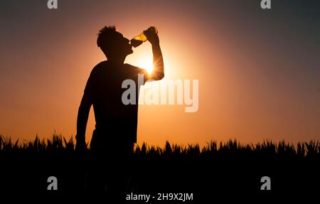 Silhouette des Menschen bei Sonnenuntergang trinkt der Mensch ein Wasser. Stockfoto