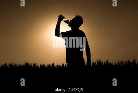 Silhouette des Menschen bei Sonnenuntergang trinkt der Mensch ein Wasser. Stockfoto