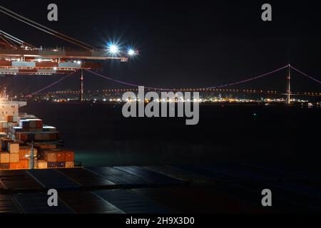 Nachtansicht vom Containerterminal mit Portalkranen und Schiffen im Hafen auf beleuchteter Aufhängung Yi Sun-Sin Bridge. Stockfoto