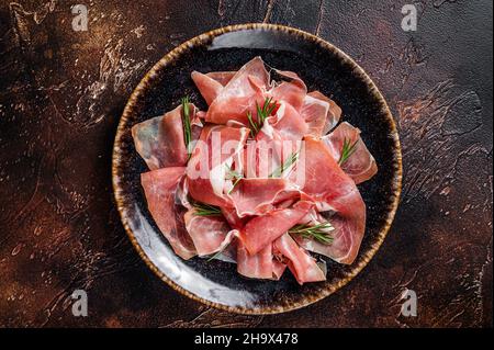 Scheiben Prosciutto crudo parma oder Jamon serrano mit Rosmarin. Dunkler Hintergrund. Draufsicht Stockfoto
