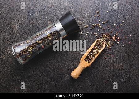 Pfeffermühle und ganzen Pfeffer in Holzlöffel auf schwarzem Tisch. Draufsicht. Stockfoto