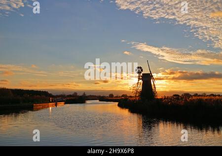 Ein Blick auf den Fluss Ant mit Sonnenuntergang hinter der Turf Fen Drainage Mill im Herbst auf den Norfolk Broads in der Nähe von Ludham, Norfolk, England, Vereinigtes Königreich. Stockfoto