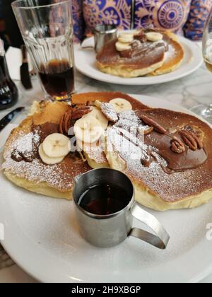 Nahaufnahme von leckeren Pfannkuchen mit Bananen, Nüssen und Schokolade auf einem Keramikplatte in einem Café Stockfoto