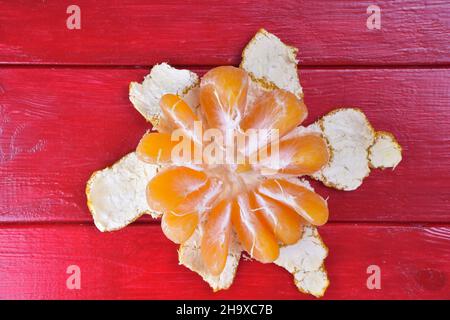 Die halbgeschälte Mandarine liegt auf einem hellroten Holzhintergrund in der Mitte des Rahmens Stockfoto