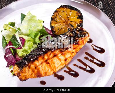 Gegrilltes Lachssteak serviert mit Sauce, gegrillter Zitrone und frischem grünen Salat Stockfoto
