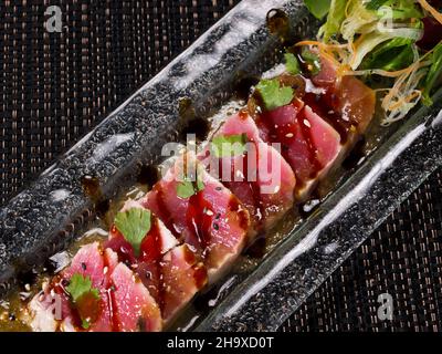 Gebratenes Thunfisch-Steak Tataki. Thunfischsteak in Scheiben in Sesam und frischem Salat. Horizontales Foto Stockfoto