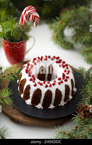 Weihnachtliches Essen. Runde Torte mit weißer Glasur. Cupcake mit einem Loch in der Mitte mit Granatapfel. Grüne Fichtenzweige auf dem Tisch. Stillleben. Süßes Gebäck, Desserts und Leckereien für das neue Jahr. Stockfoto