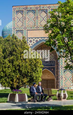 SAMARKAND, USBEKISTAN: 27. APRIL 2018: Einheimische Männer sitzen auf einer Bank vor der Bibi-Khanym-Moschee in Samarkand, Usbekistan Stockfoto