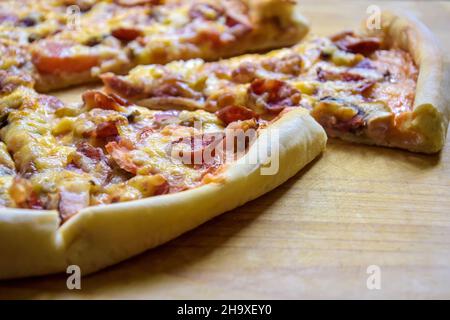 Teil einer köstlichen Pizza in Scheiben mit Oliven und Wurst auf Holzoberfläche. Nahaufnahme. Selektiver Fokus. Stockfoto