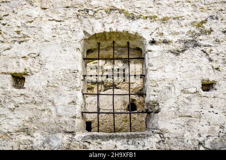 Gewölbtes Fenster mit Metallstangen in altem Mauerwerk. Die Textur des alten verfallenen Mauerwerks. Die alte halb zerstörte Synagoge. Ein Ort für religiöse r Stockfoto