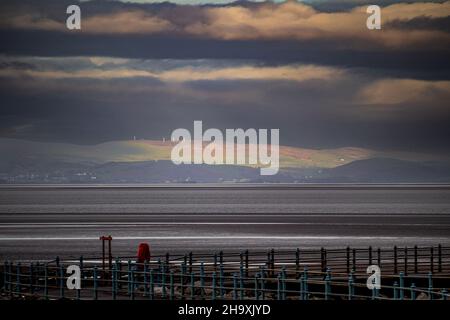 Morecambe, Lancashire, Großbritannien. 9th Dez 2021. Sonnenschein bricht durch die Wolken über Morcambe Bay, um Kirkby Moor in den South Lakeland Fells zu erleuchten Credit: PN News/Alamy Live News Stockfoto