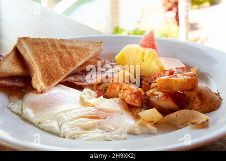 Frühstück mit Spiegeleiern, Speck, Kartoffeln, Toast und Ananas (Costa Rica) Stockfoto
