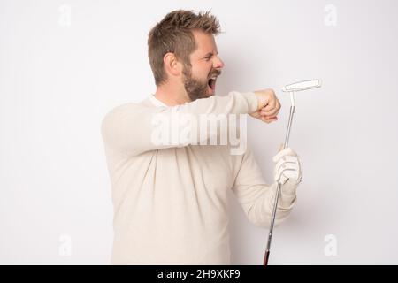 Junger, hübscher Mann, der Golf spielt, mit wütender Gesichtsfarbe, die isoliert auf weißem Hintergrund steht. Stockfoto