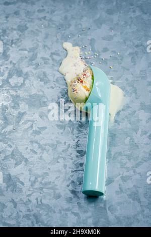 Eine Eislöffel mit einer Kugel schmelzendem Vanilleeis und Zuckerstreuseln Stockfoto