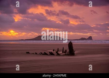 Der Himmel leuchtet rosa, als die Sonne hinter dem Schiffswrack der Helvetia aus dem Jahr 1887 am Rhossili Beach auf der Gower Peninsula in Südwales an diesem Abend untergeht Stockfoto