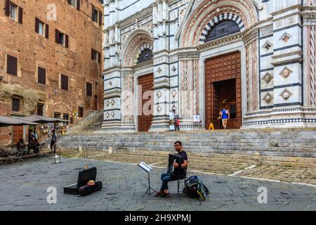 Straßenmusiker spielt Akkordeon vor der gotischen Kathedrale Santa Maria del Mariä Himmelfahrt, einer römisch-katholischen Kirche in Siena. Italien. Stockfoto