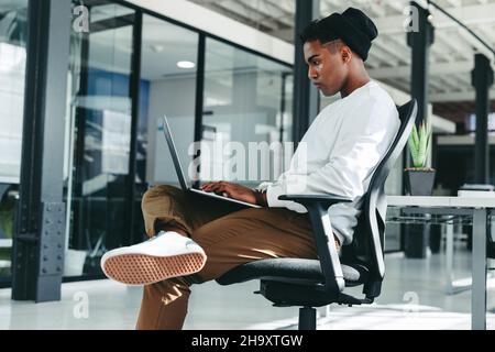 Arbeiten an einem neuen Code. Fokussierter junger Softwareentwickler, der einen Laptop verwendet, während er an einem neuen Projekt in einem Büro arbeitet. Kreativer Geschäftsmann, der alleine sitzt Stockfoto