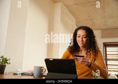 Afroamerikanische Frau, die von zu Hause aus am digitalen Tablet arbeitet und Online-Zahlungen mit Kreditkarte abgibt Stockfoto