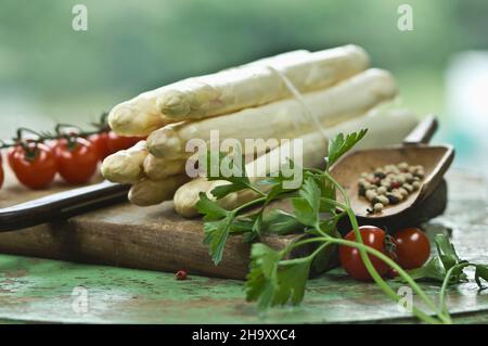 Ein Paket weißen Spargels auf einem Schneidebrett mit einem Messer, Pfefferkörnern, Petersilie und Kirschtomaten Stockfoto