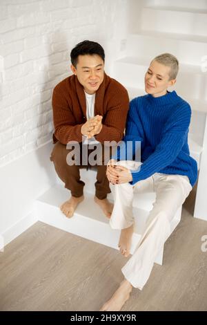 Asiatischer Mann umarmt kaukasische Frau auf Treppen zu Hause Stockfoto