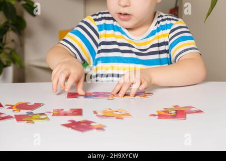 Ein Vorschulkinder spielt Puzzles, stellt ein Bild zusammen, Nahaufnahme seiner Hände. Stockfoto
