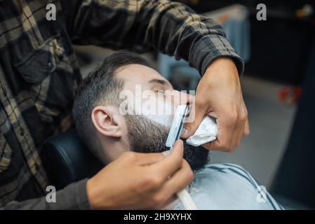 Junger bärtiger Mann wird beim Friseur im Friseursalon rasiert Stockfoto