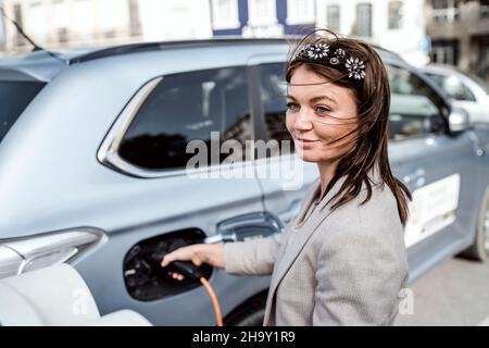 Frau lädt ein Elektroauto in städtischen Umgebungen, Faro, Portugal Stockfoto