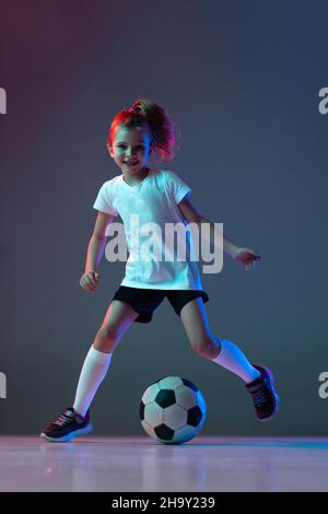 Portrait von kleinen aktiven Mädchen, Training, Dribbling Ball isoliert über Gradienten Hintergrund in Neonlicht Stockfoto