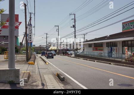 Blick auf die Hauptstraße in einer kleinen Industriestadt mit Fahrzeugen und Stromnetzkabelpfosten und klarem blauen Himmel Hintergrund. Keine Personen. Stockfoto