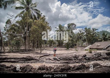 Kamar Kajang, Indonesien. 09th Dez 2021. Ein indonesischer Rettungsbeamter steht in der Nähe von Bäumen und einem mit Vulkanasche bedeckten Haus, während er in den Dörfern Kamar Kajang, Lumajang, nach Opfern sucht. Mindestens 14 Menschen sind tot und Dutzende werden verletzt, nachdem Mount Semeru, ein Vulkan in der indonesischen Provinz Ost-Java, am Samstag ausbrach und Aschetürme und heiße Wolken warf, die nahe gelegene Dörfer bedeckten. (Foto: Aditya Saputra/SOPA Images/Sipa USA) Quelle: SIPA USA/Alamy Live News Stockfoto