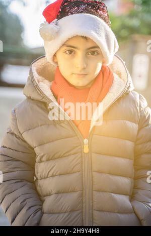 Direkter Look - Porträt eines sechsjährigen Jungen, der einen weihnachtsmannhut im Freien trägt Stockfoto