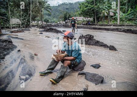 Kamar Kajang, Indonesien. 09th Dez 2021. Ein Dorfbewohner sitzt auf einem Felsen inmitten von fließendem Wasser, gemischt mit kalter Lava, nach dem Ausbruch des Berges Semeru in Kamar Kajang, Lumajang. Mindestens 14 Menschen sind tot und Dutzende werden verletzt, nachdem Mount Semeru, ein Vulkan in der indonesischen Provinz Ost-Java, am Samstag ausbrach und Aschetürme und heiße Wolken warf, die nahe gelegene Dörfer bedeckten. Kredit: SOPA Images Limited/Alamy Live Nachrichten Stockfoto