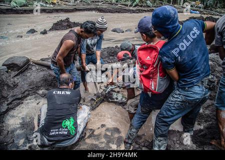 Kamar Kajang, Indonesien. 09th Dez 2021. Dorfbewohner versuchen, ein Motorrad zu entfernen, das nach dem Ausbruch des Berges Semeru in Kamar Kajang, Lumajang, von der kalten Lava begraben wurde. Mindestens 14 Menschen sind tot und Dutzende werden verletzt, nachdem Mount Semeru, ein Vulkan in der indonesischen Provinz Ost-Java, am Samstag ausbrach und Aschetürme und heiße Wolken warf, die nahe gelegene Dörfer bedeckten. Kredit: SOPA Images Limited/Alamy Live Nachrichten Stockfoto