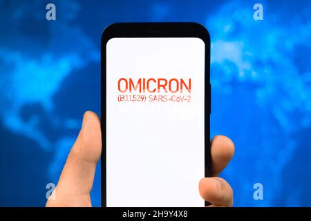 Omicron-Variante des Coronavirus. Mobiltelefon mit omicron-Text vor dem Hintergrund der Weltkarte. SARS-CoV-2, B.1.1.529. Konzept der Weltepidemie Stockfoto