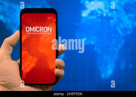 Omicron-Variante des Coronavirus. Mobiltelefon mit omicron-Text vor dem Hintergrund der Weltkarte. SARS-CoV-2, B.1.1.529. Konzept der Weltepidemie Stockfoto