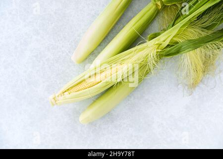 Nahaufnahme von ganz frischem, ungeschälten und geschälten Babykorn mit ungeschälten Blättern auf pastellblau strukturiertem und gemustertem Hintergrund mit Kopierraum. Draufsicht. Stockfoto