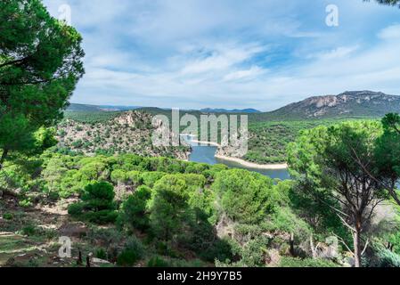 Waldlandschaft aus Kiefernwäldern, Bergen und See mit einem wolkenreichen Himmel. Ansicht von „Pantano de San Juan in San Martin de Valdeiglesias, Madrid“ Stockfoto