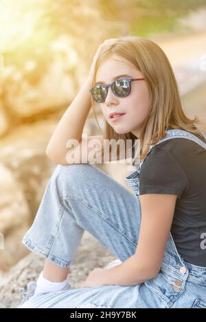 Teenager-Mädchen mit Sonnenbrille und lässiger Kleidung sitzen Blick auf den Horizont Stockfoto