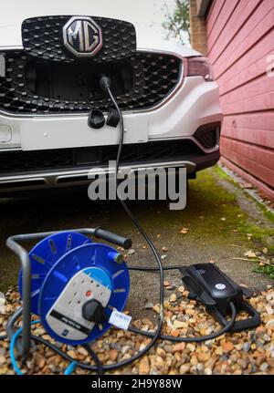 MG-Ladegerät mit einem Oma-Ladegerät mit Verlängerungskabel zu Hause laden, bestehen Hersteller darauf, keine Verlängerungskabel zu verwenden, aber viele Benutzer müssen sie verwenden. Stockfoto