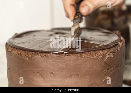 Nahaufnahme der Hand eines Kochs, der Schokoladencreme mit einem Spatel auf einem Kuchen verteilt Stockfoto