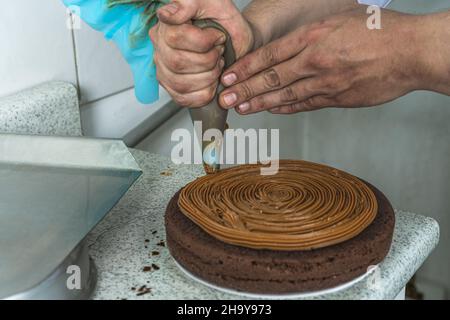 Nahaufnahme eines Konditors, der mit einem Paspelsack einen Schokoladentrüffelkuchen zubereitet Stockfoto