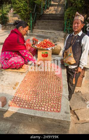 Ein Hindu-Mann und eine Hindu-Frau, die Erdbeeren und Münzen für Opfergaben im Swayambhunath-Tempelkomplex in Kathmandu, Nepal, verkaufen. Beachten Sie die kleine Schleuder Th Stockfoto