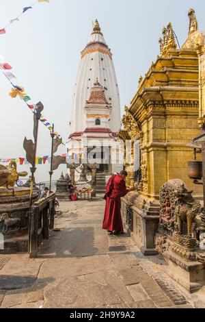 Buddhistischer Priester betet am Akshyobha Buddha an, auf der Hauptstupa. Swayambhunath Temple Complex, Kathmandu, Nepal. Dahinter steht der Shamarpas Bel aus dem Jahr 10 Stockfoto