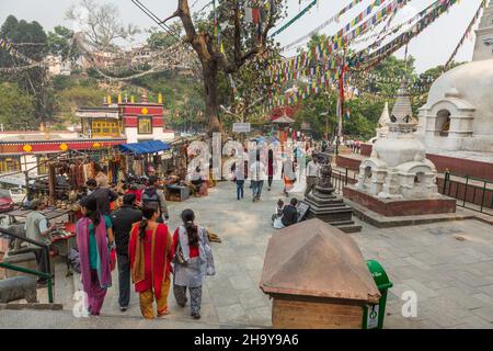 Besucher kommen im Swayambhunath-Tempelkomplex in Kathmandu, Nepal, an Verkaufsständen und buddhistischen Stupas vorbei. Stockfoto