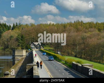 Sonnige, landschaftlich reizvolle Landschaft (Spaziergänger auf dem Bürgersteig, Autos auf der Straße, Ventilturm, Haus) - Fewston Reservoir, Washburn Valley, Yorkshire, England, Großbritannien. Stockfoto