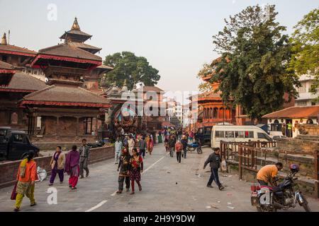 Menschen, die die Makhan Tole Street zwischen den Tempeln auf dem Durbar Square, Kathamandu, Nepal, entlang gehen. Stockfoto