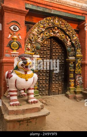 Eine steinerne weiße Löwenstatue bewacht das Singha Dhoka Gate, Durbar Square, Kathamandu, Nepal. Der Bogen um das Tor ist mit detaillierten Steinwagen bedeckt Stockfoto