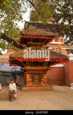 Ein nepalesischer Mann im traditionellen dhaka-Topi-Hut sitzt vor einem kleinen Tempel auf dem Durbar Square, Kathamandu, Nepal. Stockfoto