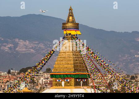 Der Turm der Boudhanath Stupa mit Gebetsfahnen und den allsehenden Augen Buddhas. Kathmandu, Nepal. Dahinter ist ein kleines Passagierflugzeug appro Stockfoto