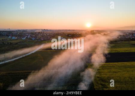 Luftaufnahme von Lagerfeuern von landwirtschaftlichen Abfällen durch trockenes Gras und Strohstoppel, die während der Trockenzeit auf Ackerland mit dichtem Rauch die Luft verschmutzen Stockfoto